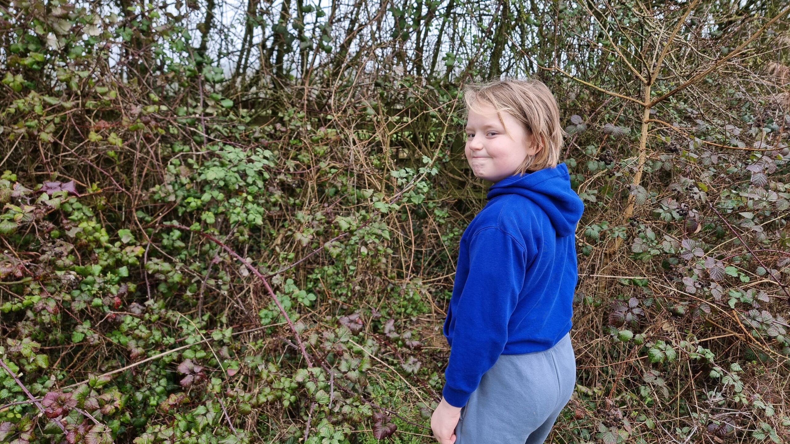 Full image of A boy looks over his shoulder as be begins to walk into a bramble bush.