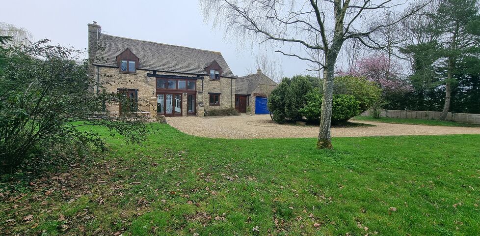 An attractive Cotswold-stone converted barn with a gravel driveway and a broad grassy lawn.