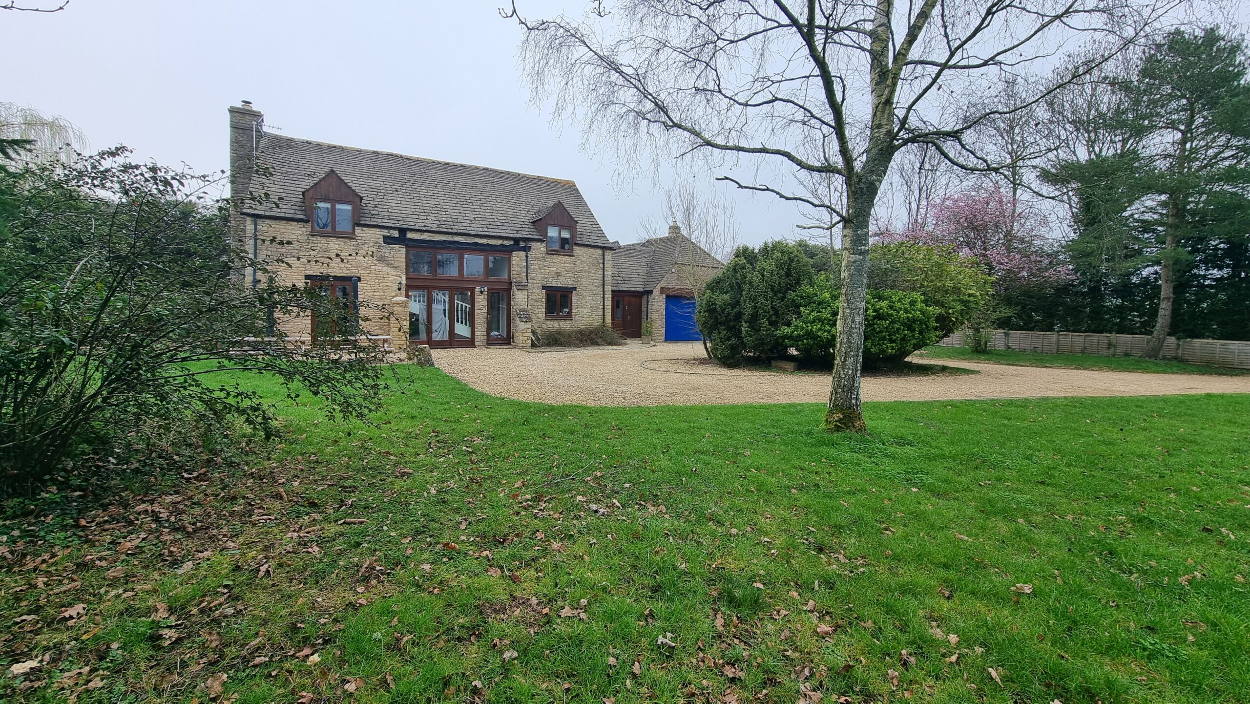 Full image of An attractive Cotswold-stone converted barn with a gravel driveway and a broad grassy lawn.