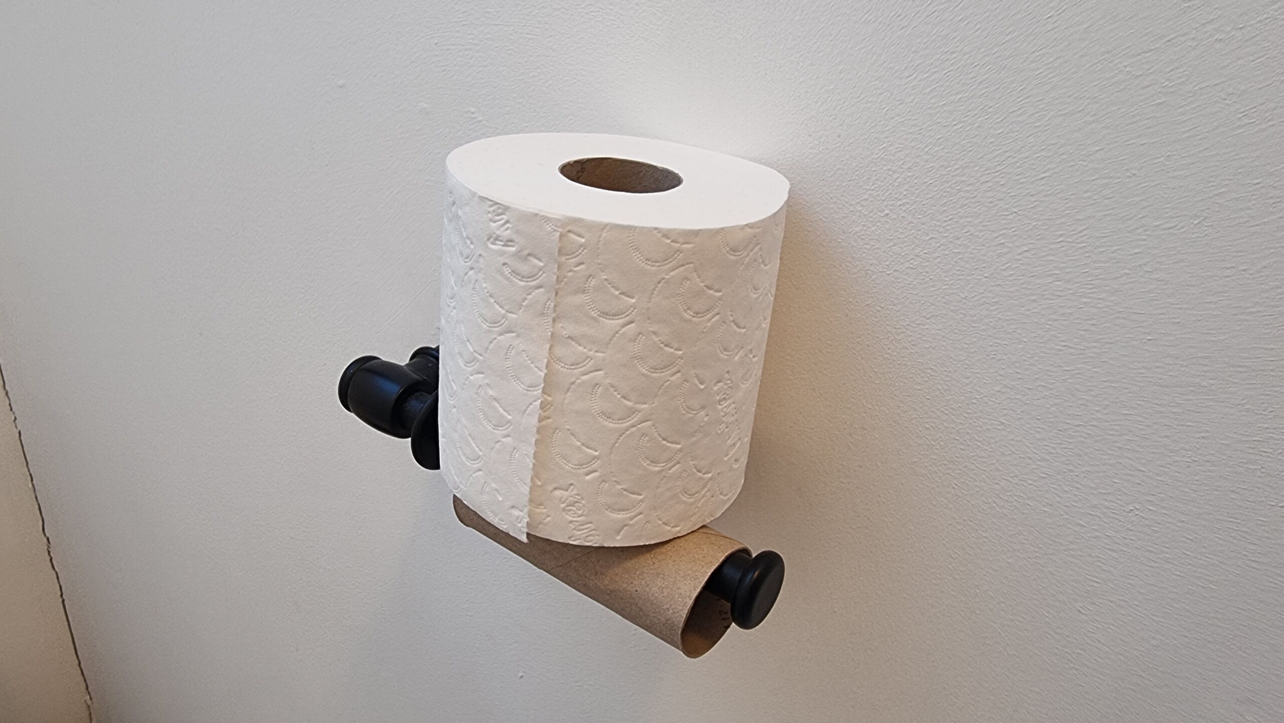 Full image of A nearly-full roll of toilet paper perched atop an empty toilet roll tube on an open-ended spindle.