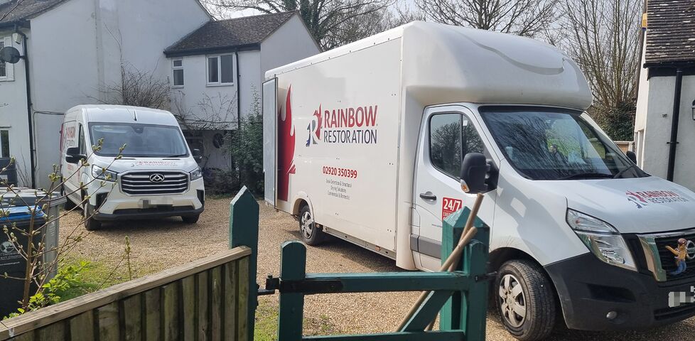 A large van and a small van from Rainbow Restoration sit on a gravel driveway.