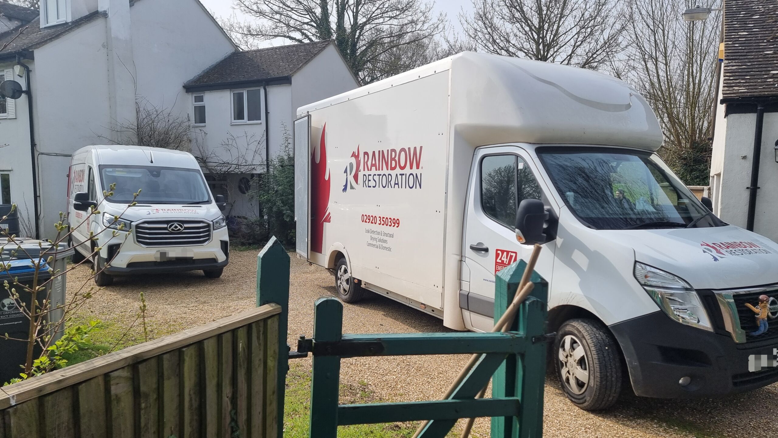 Full image of A large van and a small van from Rainbow Restoration sit on a gravel driveway.