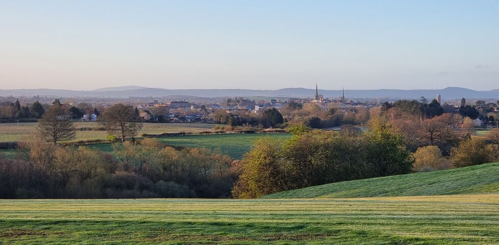 A view of Shrewsbury, from a distance, nestled in its valley, as the Spring's morning sun dapples across the verdant grass below.