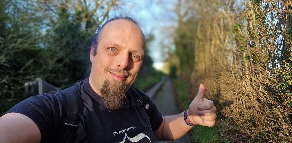 Dan throws a thumbs-up as the sun breaks through the tree-lined footpath he's walking along.