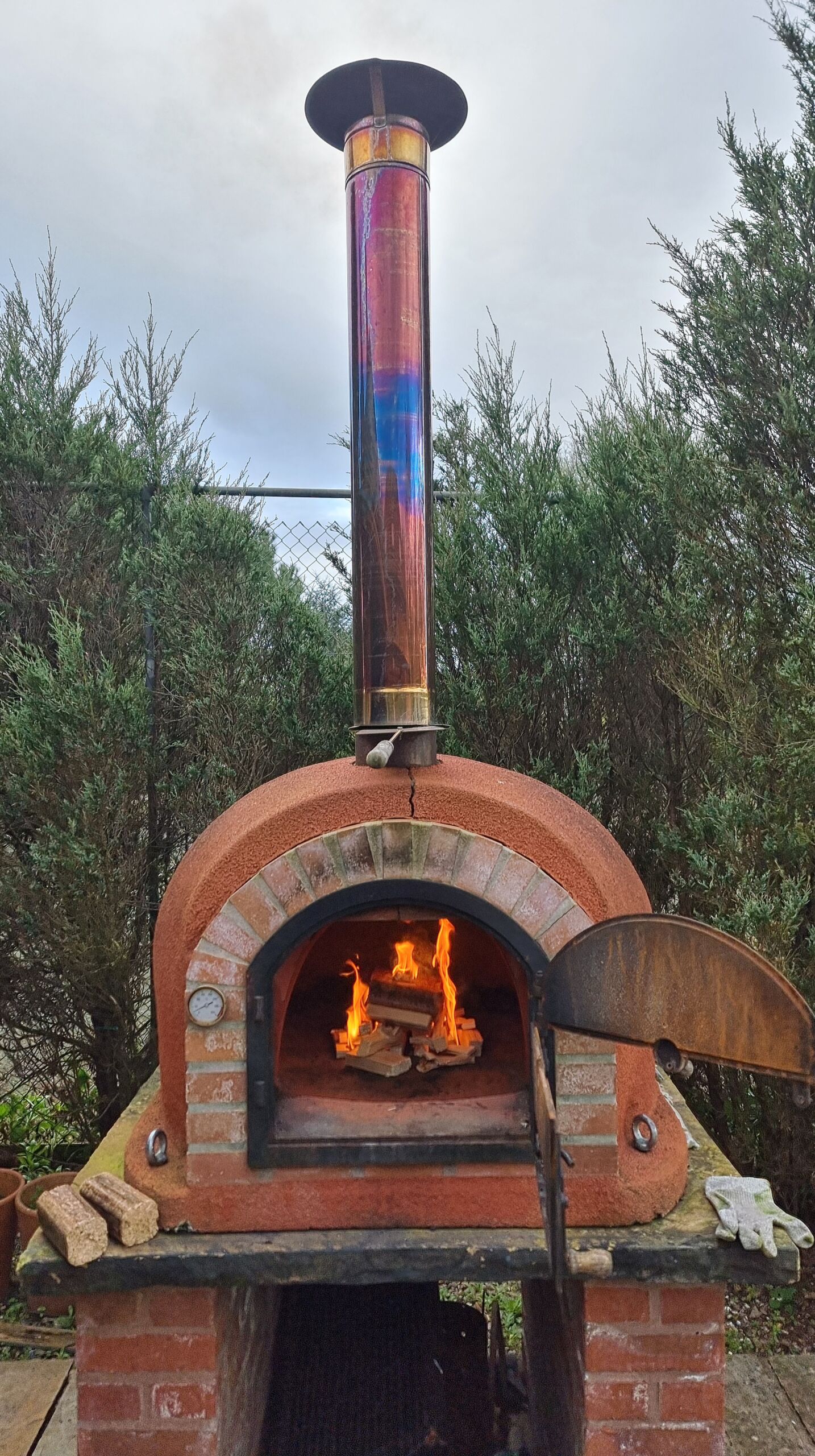 Full image of The same brick pizza oven, now seen from a few steps back with its chimney and base visible.