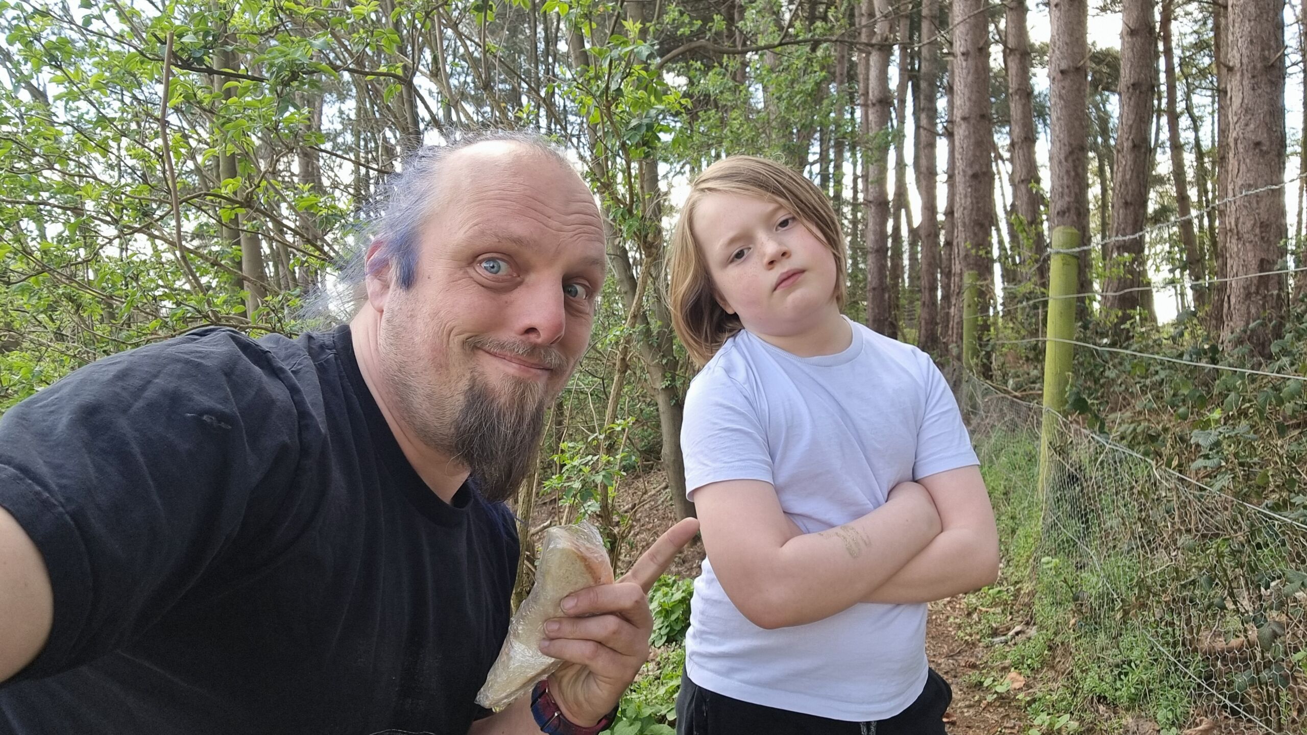 Full image of Dan and a boy holding cling-wrapped sandwiches in a forest.