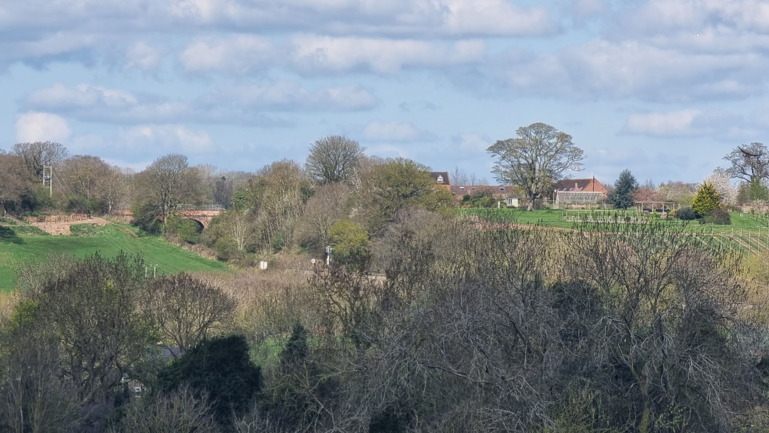 Full image of On the other side of a deep rural railway cutting, beyond a tall brick bridge, a large house stands above a vineyard.