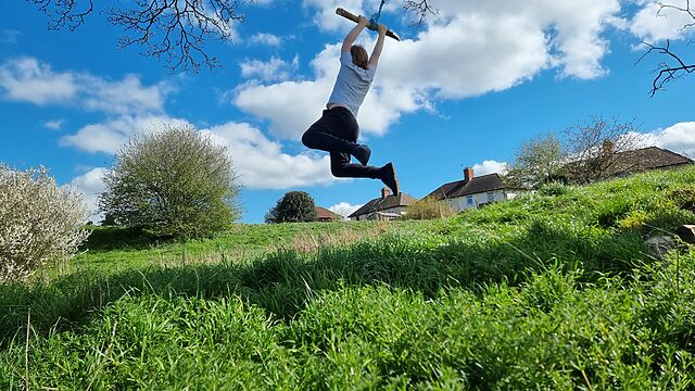 A boy hangs from a rope swing over a grassy hillside.