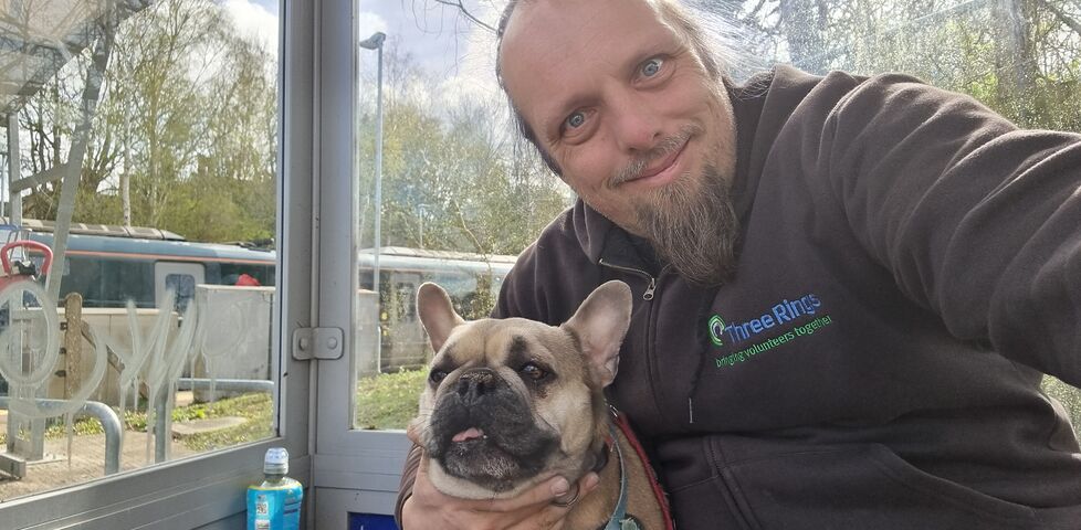 Dan sits in a glass bus shelter, hugging a French Bulldog.