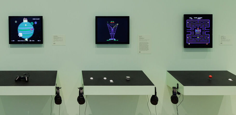 Exhibition space showing wall-mounted cabinet controls for three retro video games, from the header of Mike Cook's original article.
