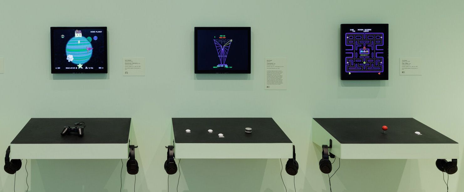 Full image of Exhibition space showing wall-mounted cabinet controls for three retro video games, from the header of Mike Cook's original article.
