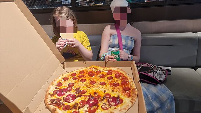 Two preteen children sit in front of an enormous pepperoni pizza.