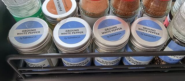 Close-up of a spice rack containing not one, not two, not three but four tubs of 'ground white pepper by Sainsburys'.