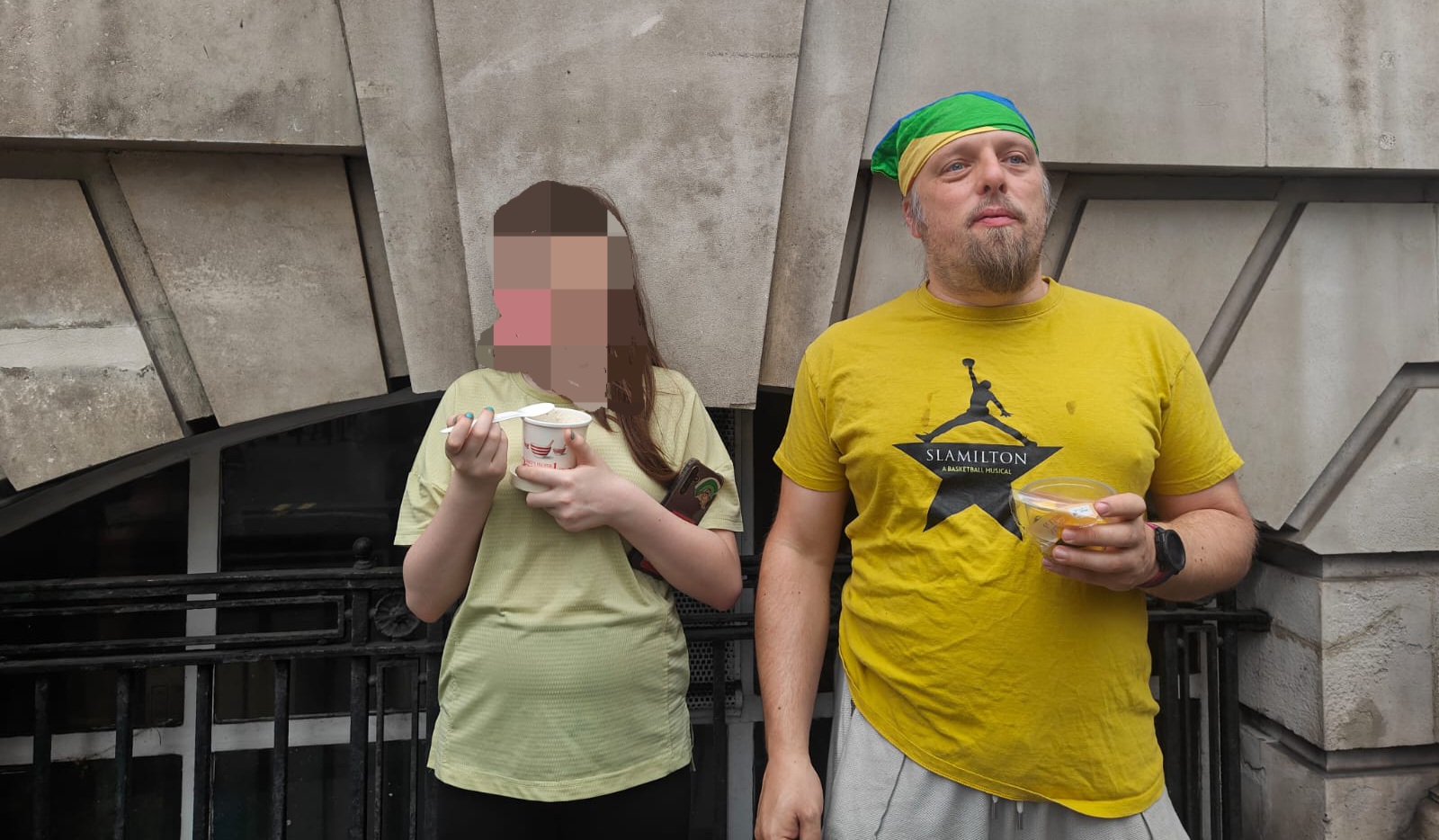 Full image of Dan, wearing a Slamilton t-shirt, stands with a tweenager outside a Central London building.