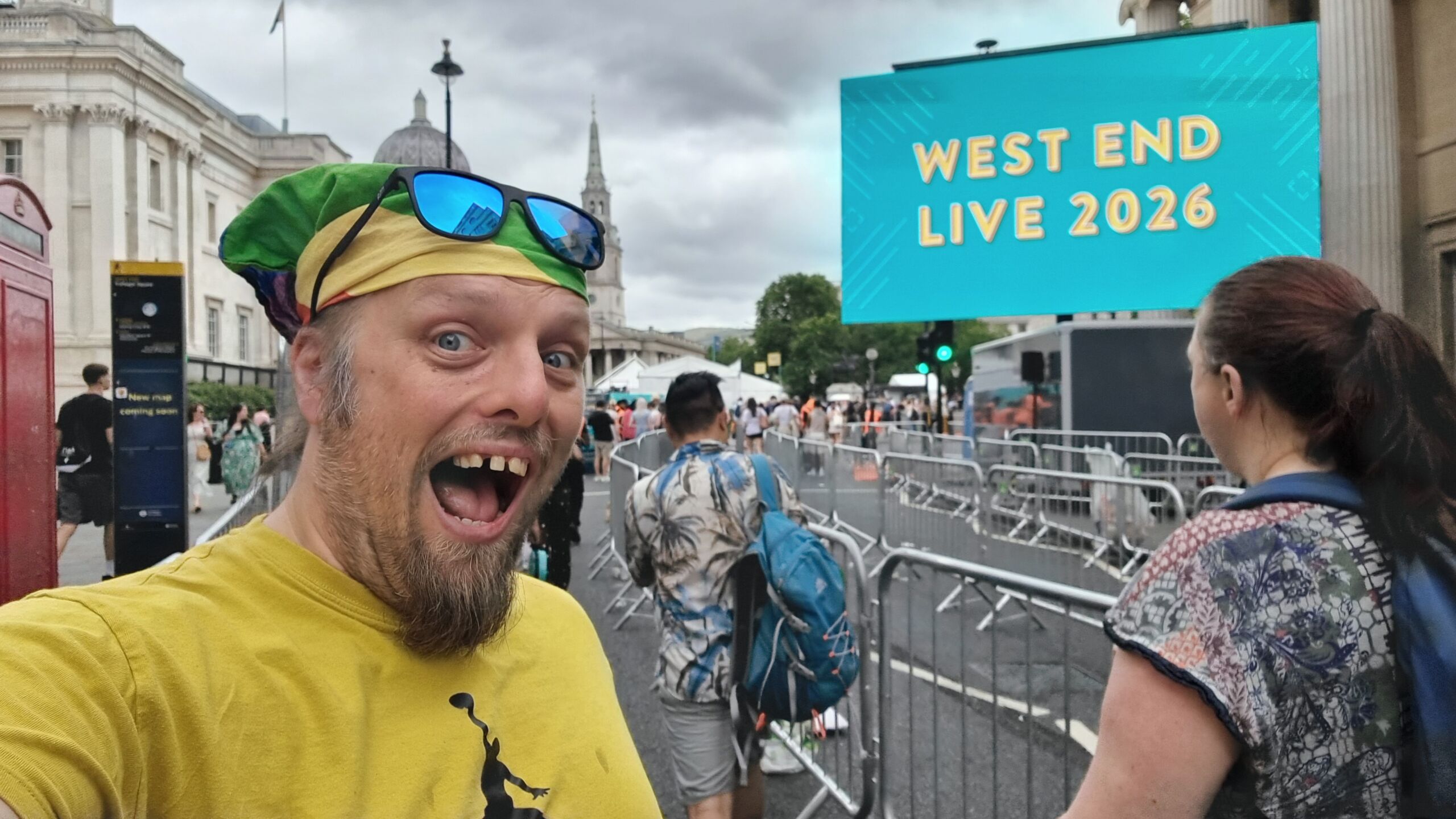 Full image of Dan, near the front of a long queue, in front of an illuminated West End Live sign.
