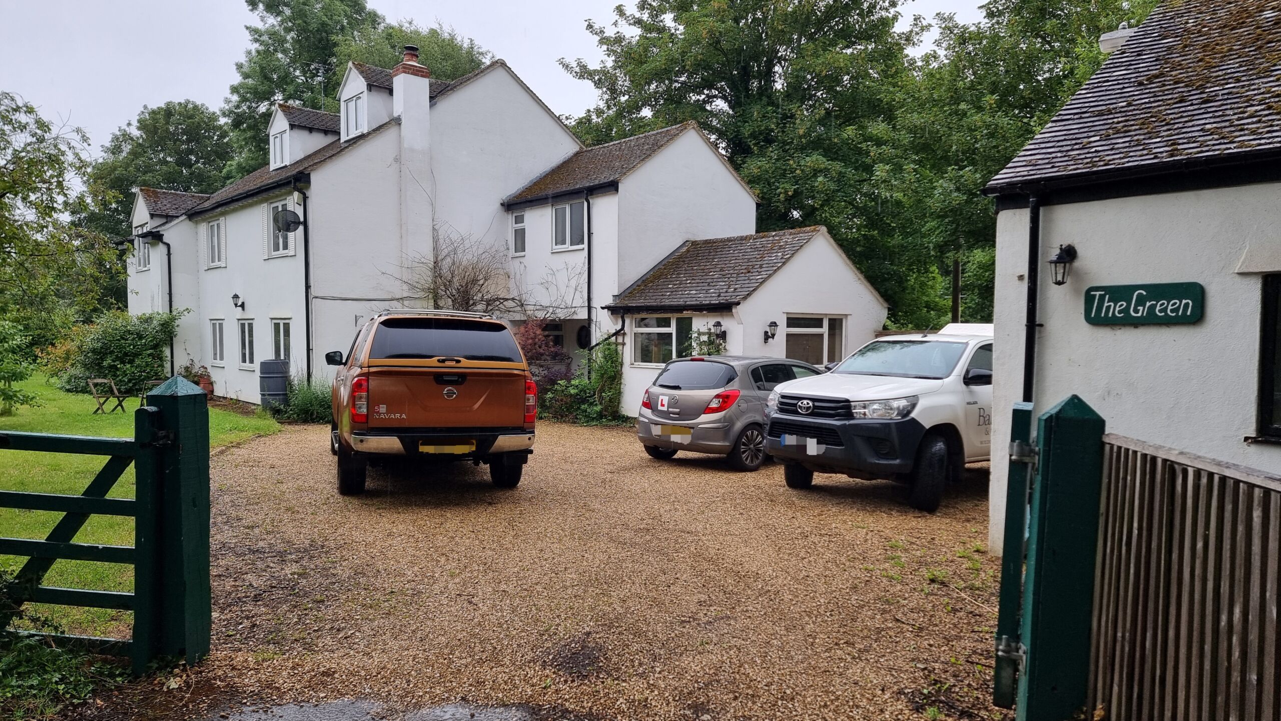 Full image of Several vehicles parked in the rain on the rural residential driveway of 'The Green'.