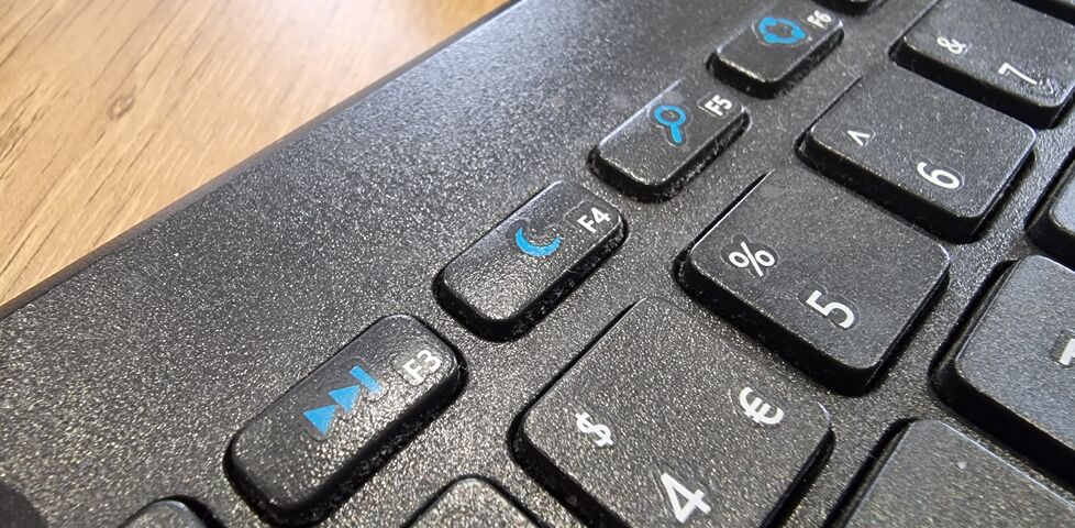 Close-up of the F4 key of a multi-function slim wireless keyboard, showing a 'moon' icon. Of the other visible function keys, F3 shows 'fast forward', F5 shows 'hourglass', F6 shows what appears to be an illustration of a supercollider spinning up, and so on.