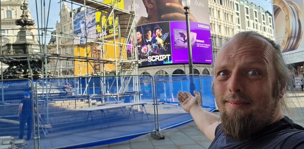 Dan stands in front of a scaffolded fountain at the iconic Piccadilly Circus.