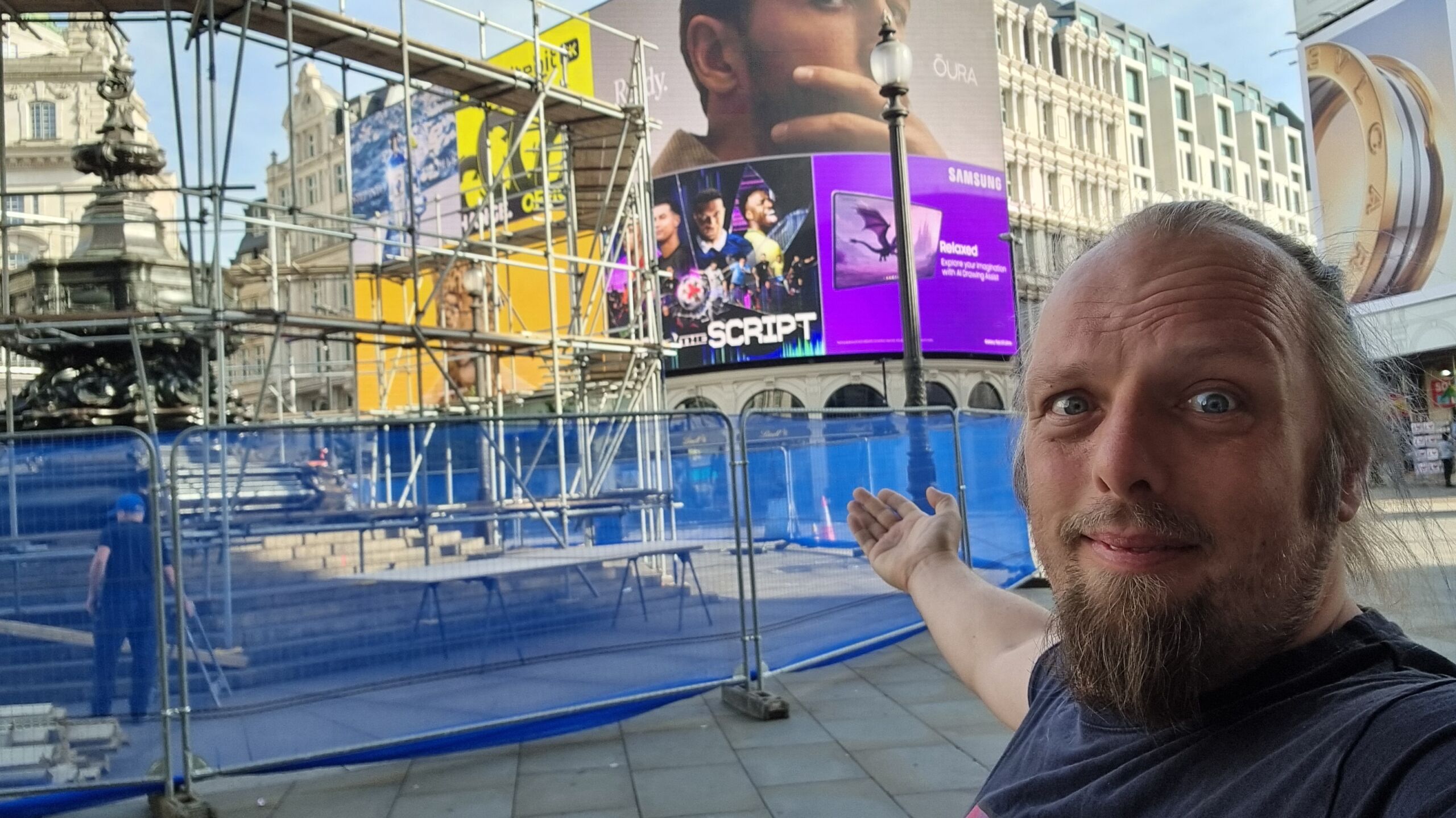 Full image of Dan stands in front of a scaffolded fountain at the iconic Piccadilly Circus.