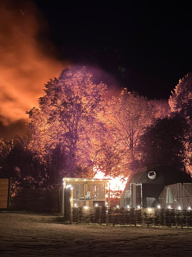 A static caravan is engulfed in flames behind a dome tent, at night.
