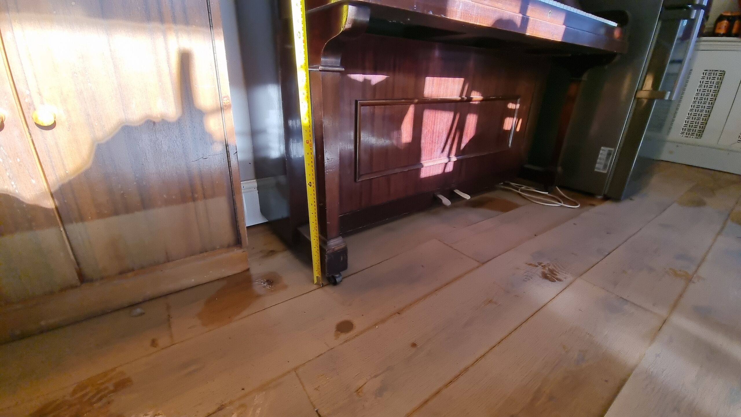 Full image of Post-flood photo of the body of an upright piano alongside a cabinet with a clear tide mark up to about a foot from the ground.