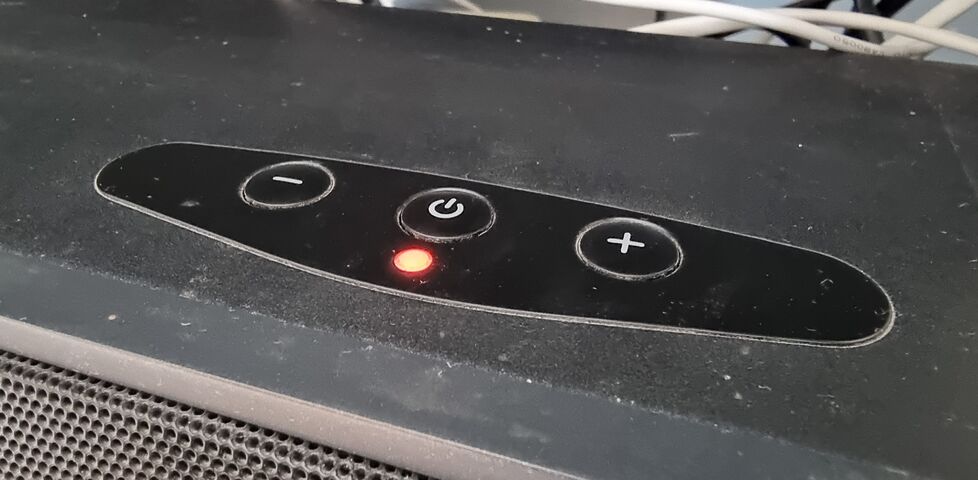 Top surface of a TV soundbar showing plus, minus, and power buttons, and a red LED.