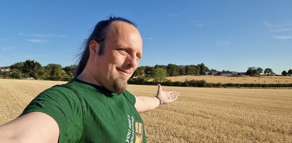 Standing in a field, Dan raises his arms in victory.