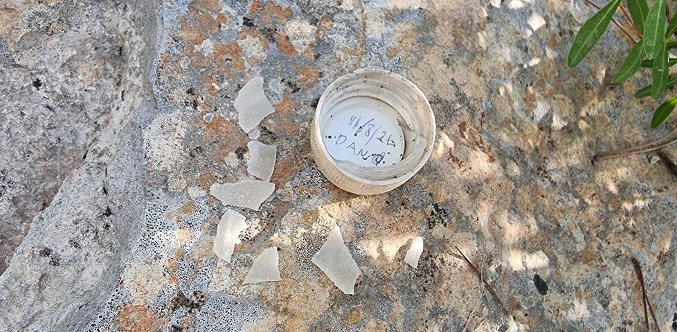 A bottle top style lid, with Dan's name written in it, sits alongside some plastic shards on top of a rock.