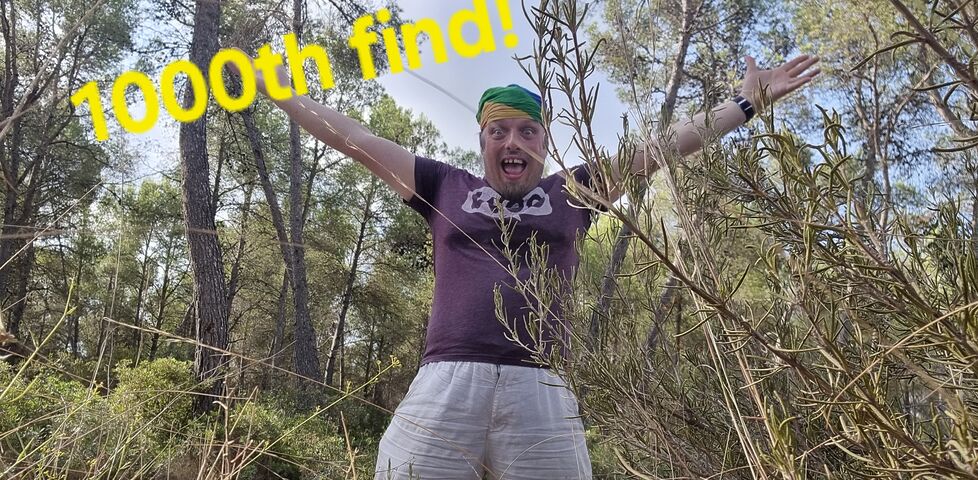 Dan - a white man wearing a rainbow-striped bandana - stands with his arms raised in celebration, alongside the superimposed words '1000th find'.