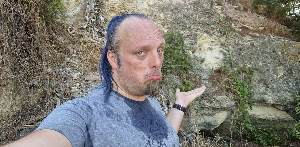 Dan, dripping with sweat, stands half-way up a cliff face.