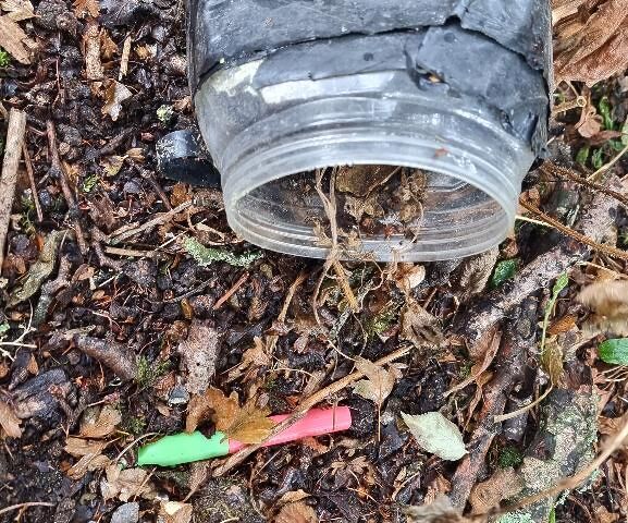 A badly damaged geocache with a toy whistle falling out of it.