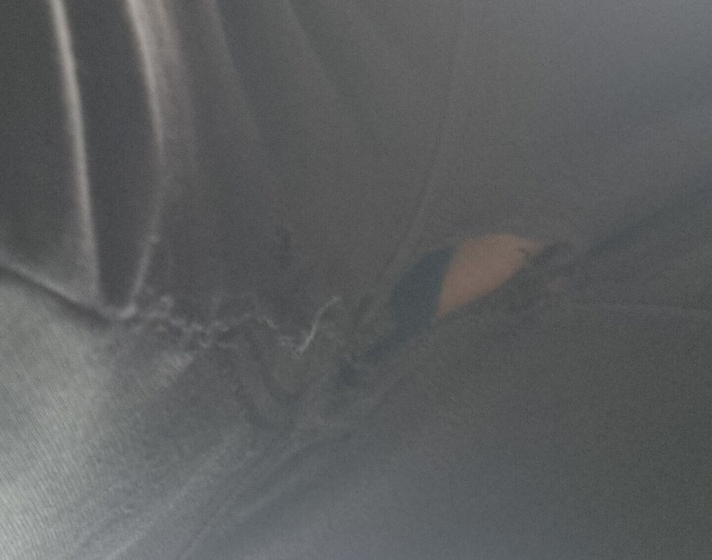 Full image of Close-up of the crotch of a pair of black tracksuit bottoms, with some skin and underwear visible through a small hole.