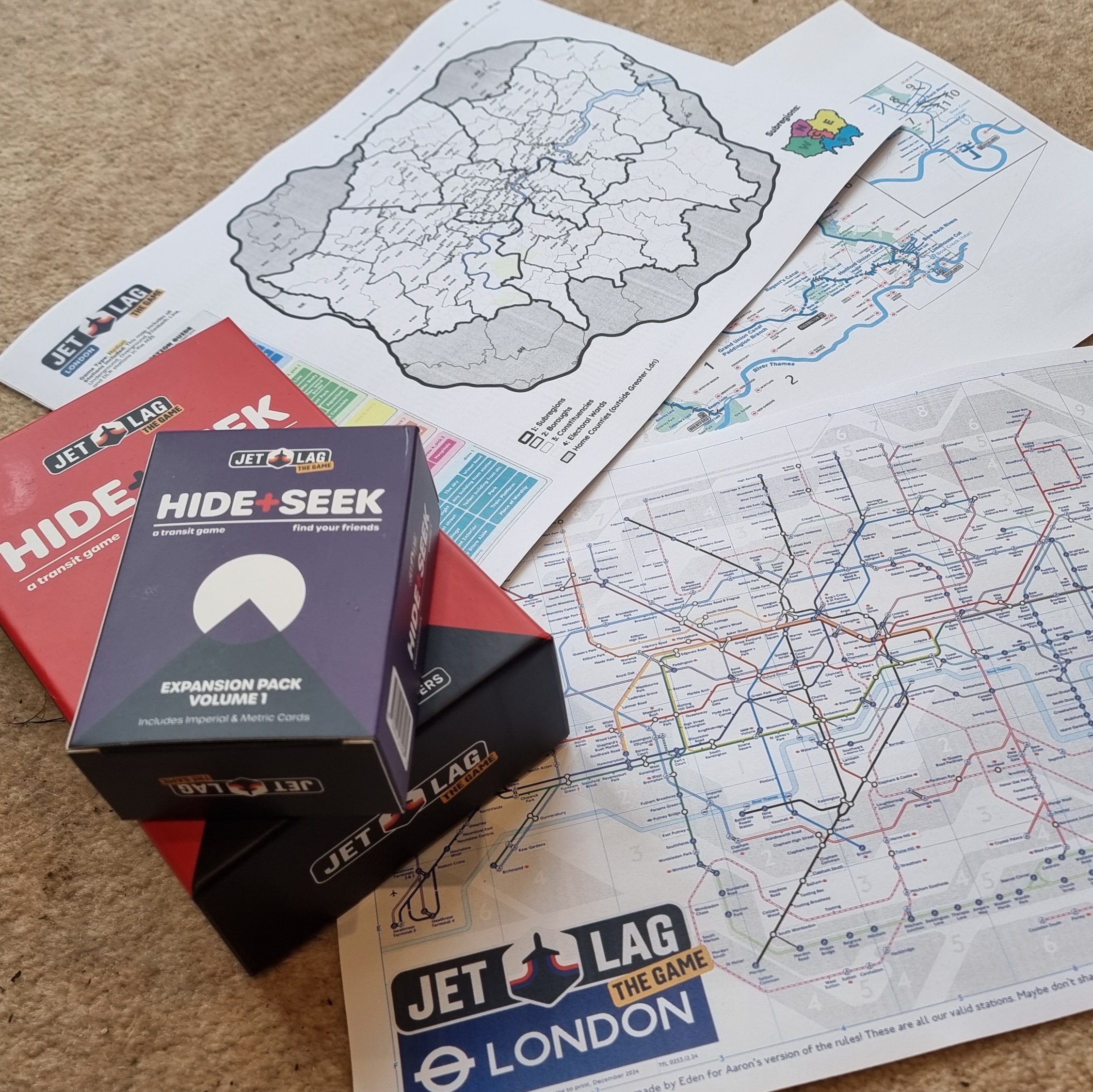 Full image of Customised maps of Greater London's transit network alongside a boxed set of Jet Lag: The Game - Hide & Seek and its expansion.