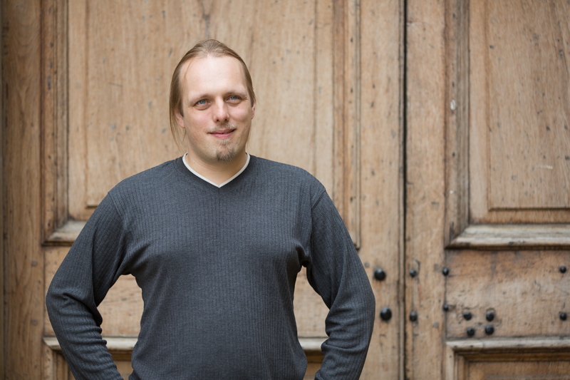 Full image of Dan, aged in his 30s, looks up at the sky outside a large wooden door.