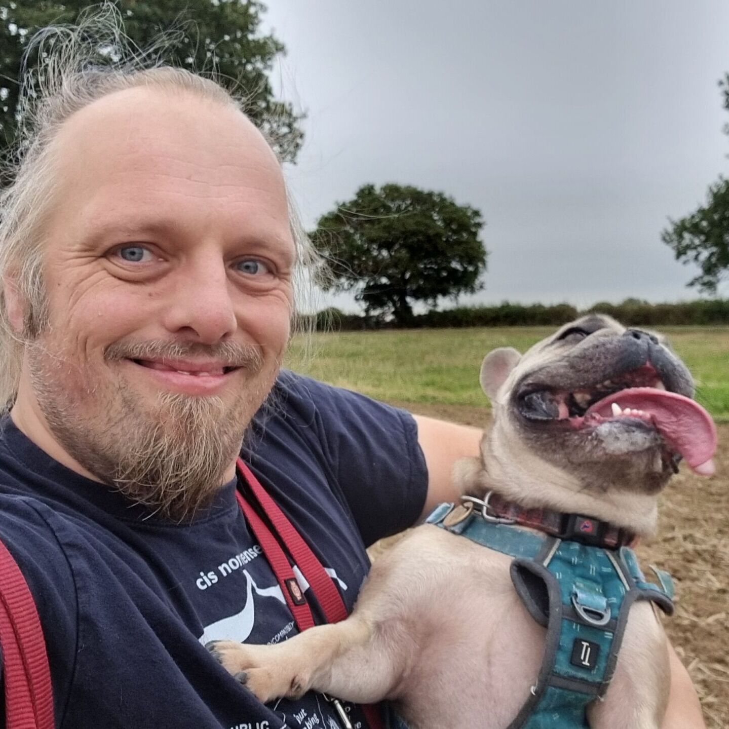 Full image of A French Bulldog with her tongue hanging out is lifted by Dan.