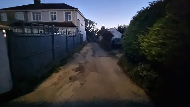 A disreputable-looking cycleway leads between houses into the distance, in the early morning light.