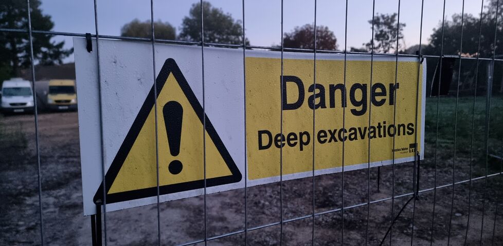 A 'danger: deep excavations' sign on a wire fence.