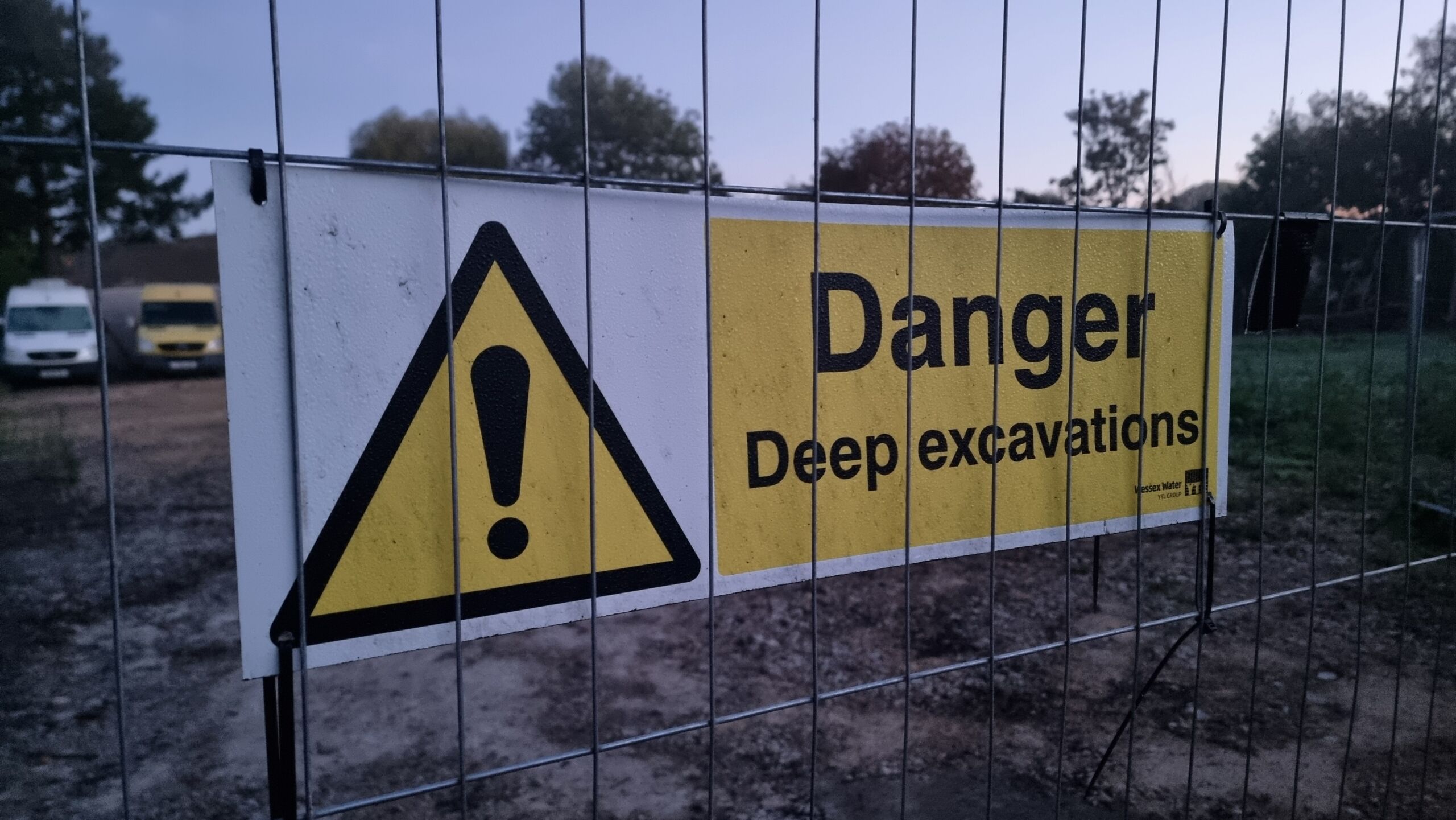 Full image of A 'danger: deep excavations' sign on a wire fence.
