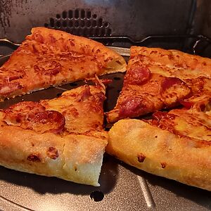 Four slices of pepperoni pizza reheat in an oven.