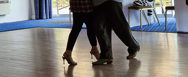 Legs of a couple dancing tango on a polished wooden floor.