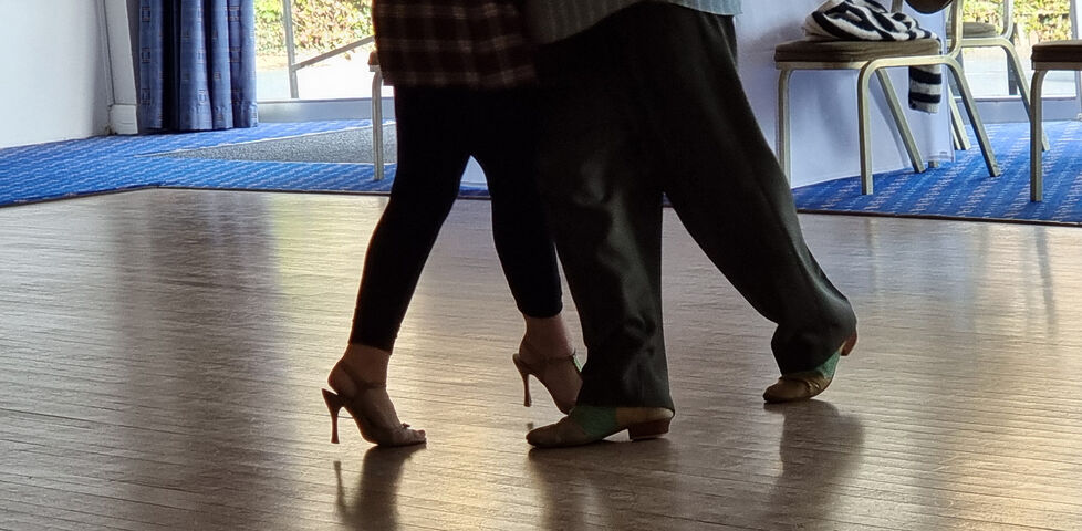 Legs of a couple dancing tango on a polished wooden floor.