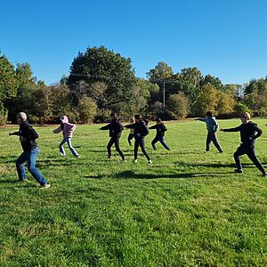 In a grassy meadow, a group of martial arts students hold a warrior pose.
