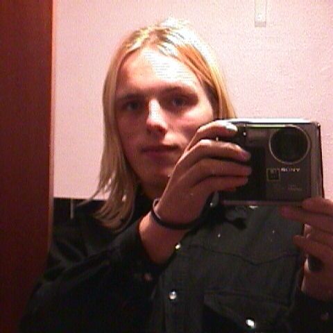 Dan, with exceptionally-blonde hair, holds a large square digital camera.