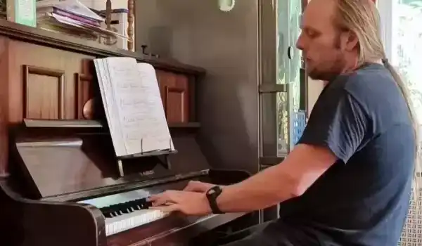 Dan, wearing a black t-shirt and tracksuit bottoms, playing an upright piano.